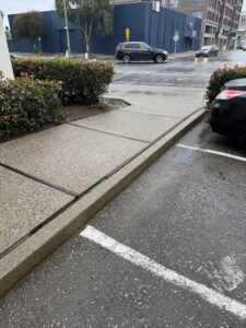 A concrete sidewalk, curb, and street area needing pressure washing to remove grime and stains from the public right-of-way.