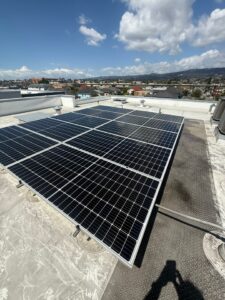 A Spotfree Window professional using a water-fed pole to clean a rack-mounted commercial solar panel system on a white flat roof.