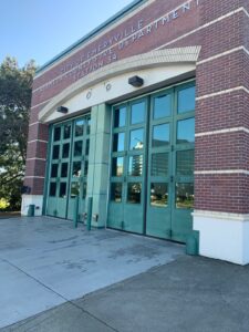 The exterior of a city fire station with large green garage doors and windows, cleaned by Spotfree Window's professional window washing service.