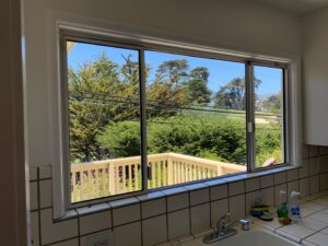 A clean kitchen window looking out over a white railing and garden, showing the brilliant results of a professional residential window washing service.