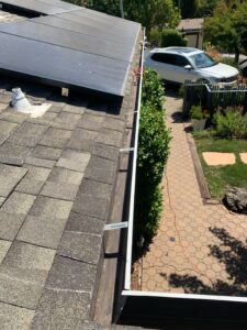 Spotfree Window gutter cleaning in progress, showing a long run of gutters directly underneath a residential solar panel array and overlooking a driveway with a white SUV.