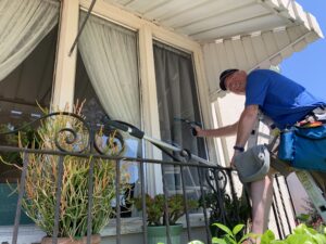 A friendly technician in a blue shirt on a ladder, ready to professionally wash the windows of a residential home.