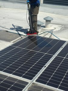 Close-up view of a Spotfree Window technician using a soft brush and purified water to clean dirty solar panels, showing the dramatic difference between the cleaned and dirty sections.