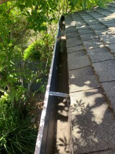 The final result of Spotfree Window's gutter cleaning service, showcasing a pristine and completely clear interior gutter with sunshine casting shadows through nearby trees.
