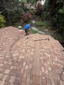 A Spotfree Window technician preparing for gutter cleaning on a residential shingle roof near a brick chimney, with safety cords and tools laid out.