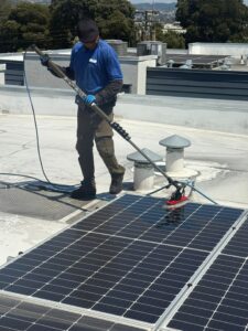 A certified Spotfree Window technician using a long carbon-fiber pole system to safely wash commercial solar panels on a flat rooftop.