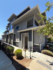 A multi-story, modern grey townhouse with dark window trims and a clean front entrance after a professional whole house washing by Spotfree Window.