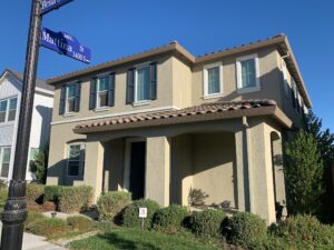 A two-story tan home with dark shutters and a clean exterior after a full whole house washing service by Spotfree Window.