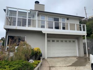 A clean residential home with grey stucco exterior, windows, and a glass balcony after a complete whole house washing by Spotfree Window.