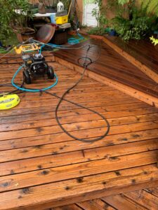 A professional pressure washer, hoses, and surface cleaner set up on a large wooden deck ready for power washing by Spotfree Window.